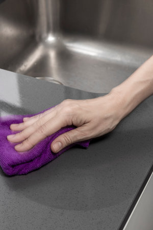Person cleans a kitchen countertop with a purple cloth near a stainless steel sink