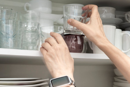 Person reaching to place or take drinking glasses from an organized kitchen shelf