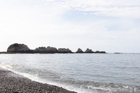 Gentle waves approaching a pebble beach with weathered rocks along the coast of asturias