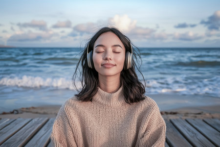 Young woman with closed eyes enjoying music and peaceful moments on beachの素材