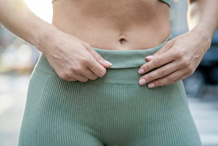 Woman's hands adjusting green ribbed athletic leggings with a flat stomach and belly buttonの素材
