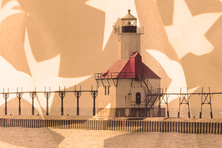 Double exposure St. Joseph north pier lighthouse along shoreline of Lake Michigan with American flag backgroundの写真素材