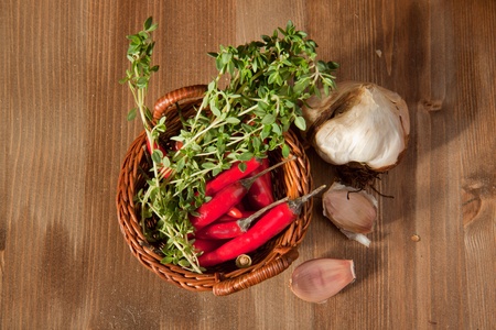Basket of red hot chili peppers with herbs and onion on the wooden backgroundの写真素材