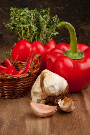 Red paprika, basket of chili pepper, onion and fresh herb on the wooden tableの写真素材