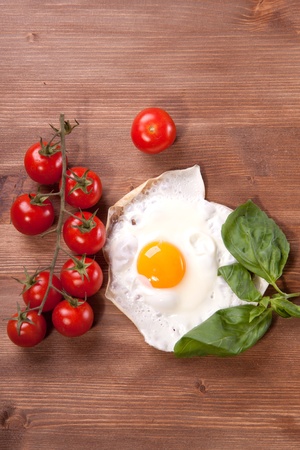 Fried egg served on a wooden table with tomato and fresh herbsの写真素材