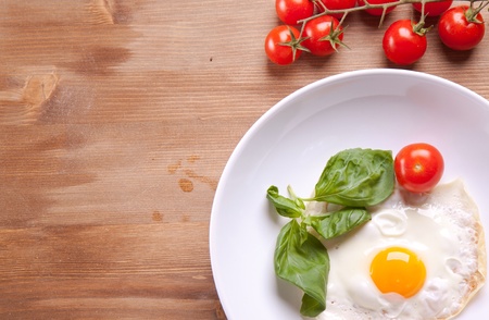 Fried egg served on a wooden table with tomato and fresh herbsの写真素材