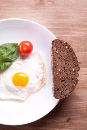 Fried egg served on a wooden table with tomato and fresh herbsの写真素材