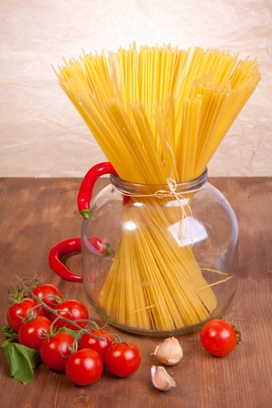 Bunch of spaghetti in the glass pot with cherry tomato, chili peppers and onionの写真素材