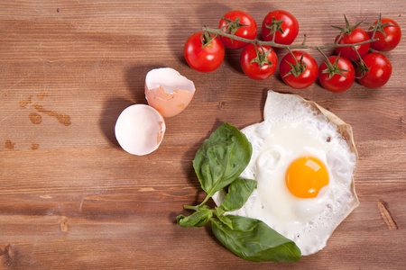 Fried egg served on a wooden table with tomato and fresh herbsの写真素材