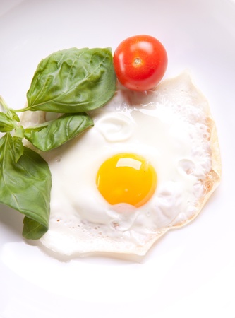 Fried egg served on a white plate with tomato and fresh herbsの写真素材