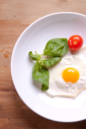 Fried egg served on a white plate with tomato and fresh herbsの写真素材