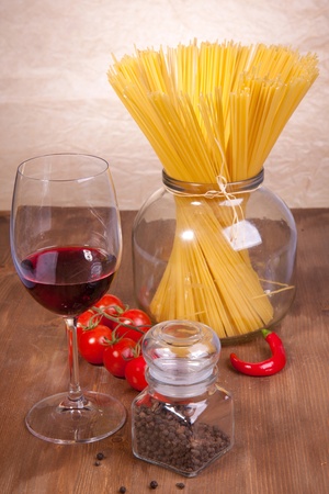 Composition of pasta, pepper, tomato and glass of red wine on the wooden tableの写真素材