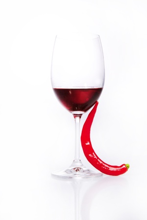 Glass of red wine with red hot chili pepper over whiteの写真素材