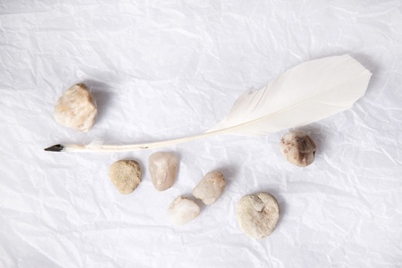 White feather and river stones on white crumpled paper の写真素材