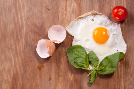 Fried egg served on a wooden table with tomato and fresh herbsの写真素材