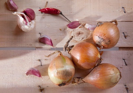 Onion, garlic and pepper on a wooden desk in sun shineの写真素材