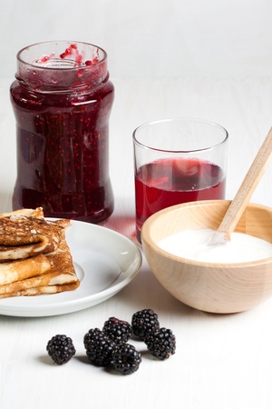 Breakfast with pancakes, yogurt  and blackberries, served on white table with glass of juiceの写真素材