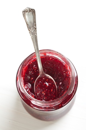 Raspberry jam in glass with silver spoon on white tableの写真素材