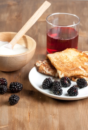 Breakfast with pancakes, yogurt  and blackberries, served on wooden table with glass of juiceの写真素材