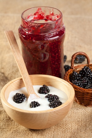 Wooden bowl of Yogurt and blackberries with pot of jam on sackclothの写真素材