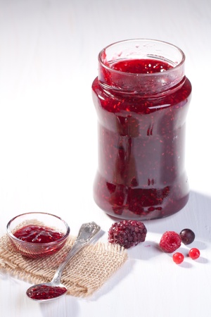 Raspberry jam in glass with silver spoon and fresh berries on white tableの写真素材