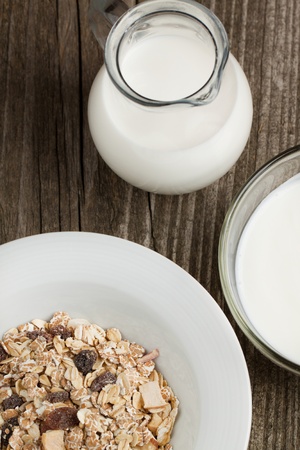 Top view to bowls of yoghurt and muesli with jug of milk on old wooden deskの写真素材