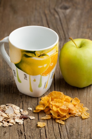 Green apple with muesli and corn-flakes and colorful cup on old wooden tableの写真素材