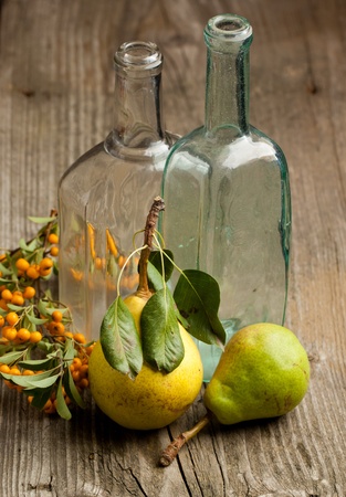 Composition with fresh pears, orange berries and tow vintage glass bottle on old wooden tableの写真素材