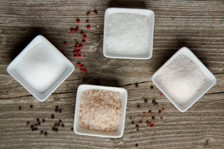 Four kind of salt in white plates and peppers on old wooden table