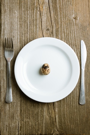 One quail raw egg in white plate with tableware on old wooden tableの写真素材