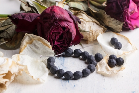 beautiful black beads on white wooden table with dried red and white rosesの写真素材
