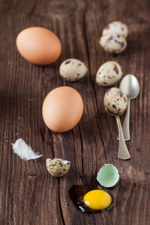 Broken quail egg with the leaked yolk and chicken eggs on old wooden tableの写真素材