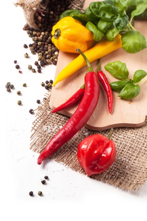 Red and yellow hot chili peppers with salt and fresh basil over whiteの写真素材