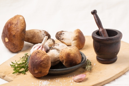Heap of cep mushrooms with garlic, thyme and vintage  mortar on wooden cutting boardの写真素材