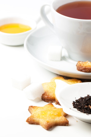Cup of black tea served with homemade sugar cookies and dry tea leaves over whiteの写真素材