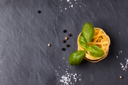 Top view on dry pasta and fresh basil served with sea salt on dark gray backgroundの写真素材