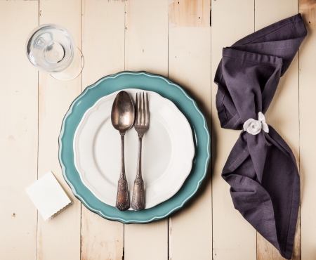 Top view on table setting with vintage silverware on white and turquoise plates with blank guest...