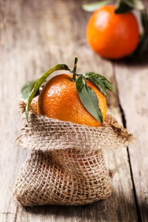 One tangerine with leaves in sack on old wooden の写真素材