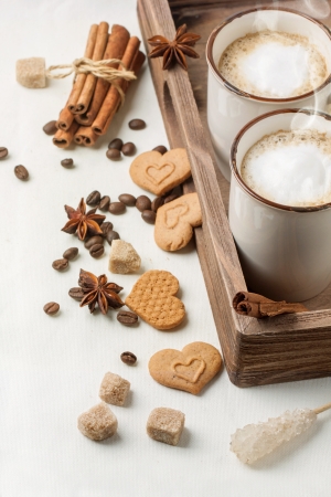 Tow cup of cappuccino served with spices and cookies as hearts on white textileの写真素材