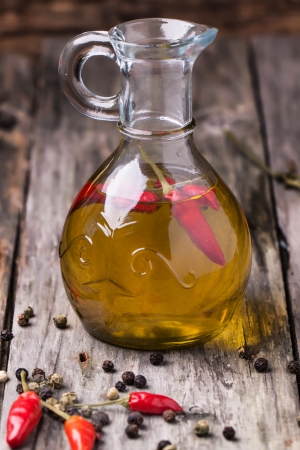 Glass bottle of olive oil with red hot chili peppers over old wooden background. See seriesの写真素材