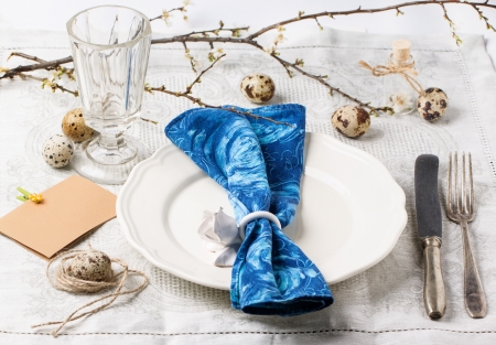Easter table setting with vintage silverware, white plate, blue textile napkin, quail eggs and...