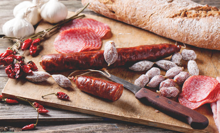 Set of salami sausages served with fresh bread, garlic and red hot chili peppers on wooden cutting board. See series.の写真素材