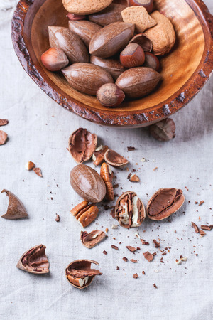 Wooden bowl with whole and chopped pecan nuts over gray textile. の写真素材