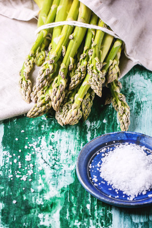 Bunch of young green asparagus with ceramic plate of sea salt over green wooden table. See seriesの写真素材