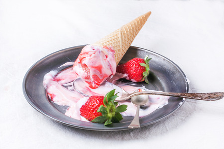 Wafer cones with strawberry ice cream with syrup, spoons and fresh strawberries served on vintage plate over white textile. See seriesの写真素材