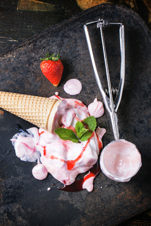 Wafer cone with strawberry ice cream with fresh strawberries, mint and metal spoon over black table. Top view.の写真素材