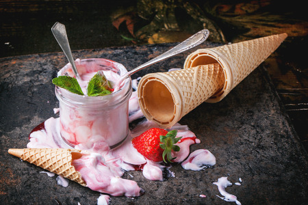 Strawberry ice cream with mint and fresh strawberries served in glass jar with empty wafer cones...