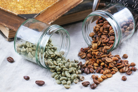 Glass jars with green and brown decaf unroasted coffee beans on table with vintage books