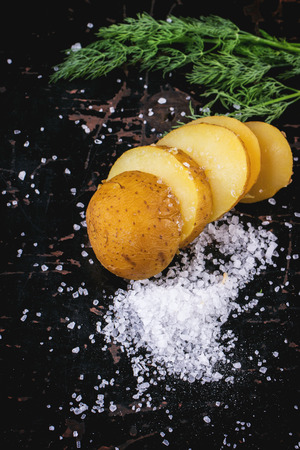 Sliced boiled potatoes with sea salt and dill over black wooden tableの写真素材