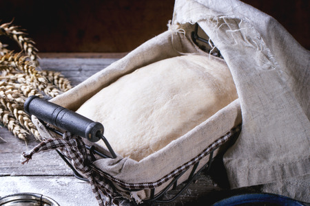 Baking bread. Dough in proofing basket on wooden table with flour and wheat ears.の写真素材